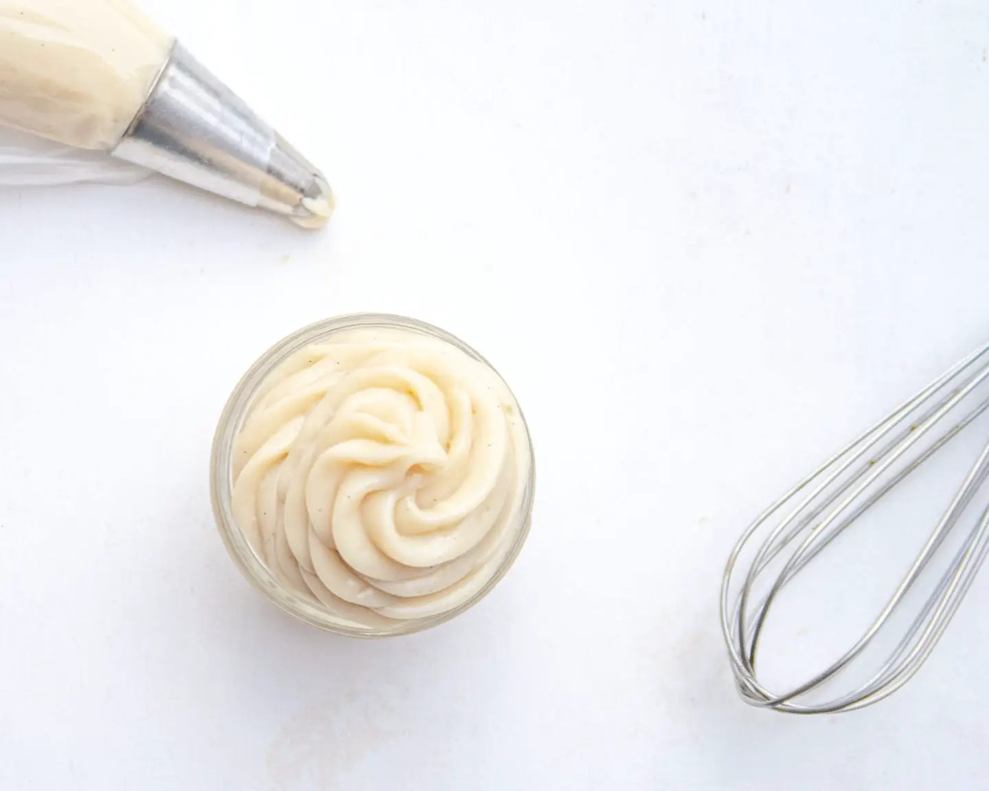 Top view of vegan pastry cream in a jar with a whisk and pastry bag
