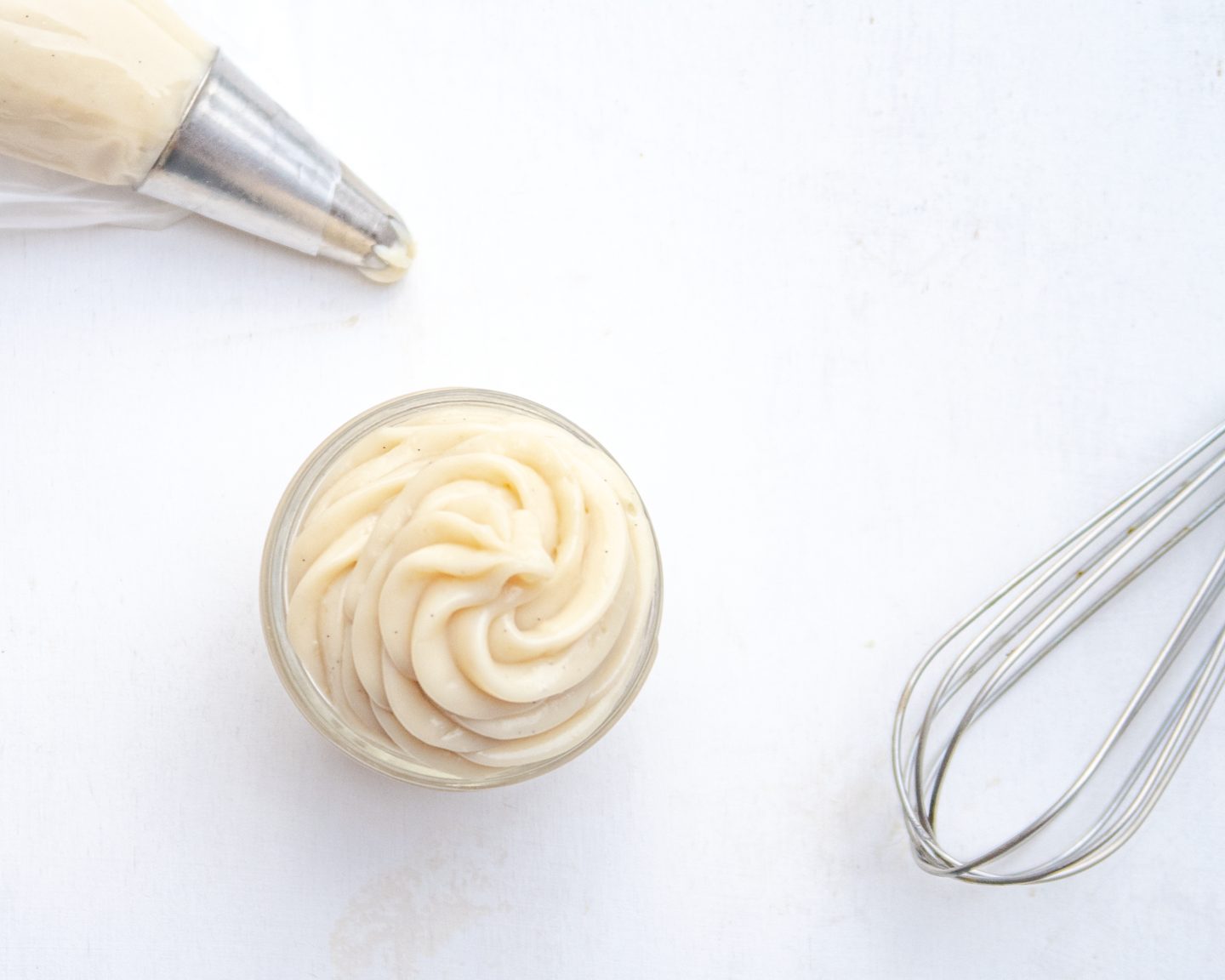 Top view of vegan pastry cream in a jar with a whisk and pastry bag