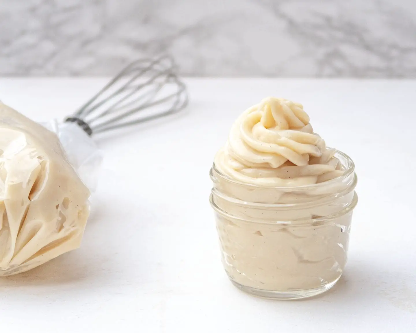 side view of vegan pastry cream in a jar with a whisk