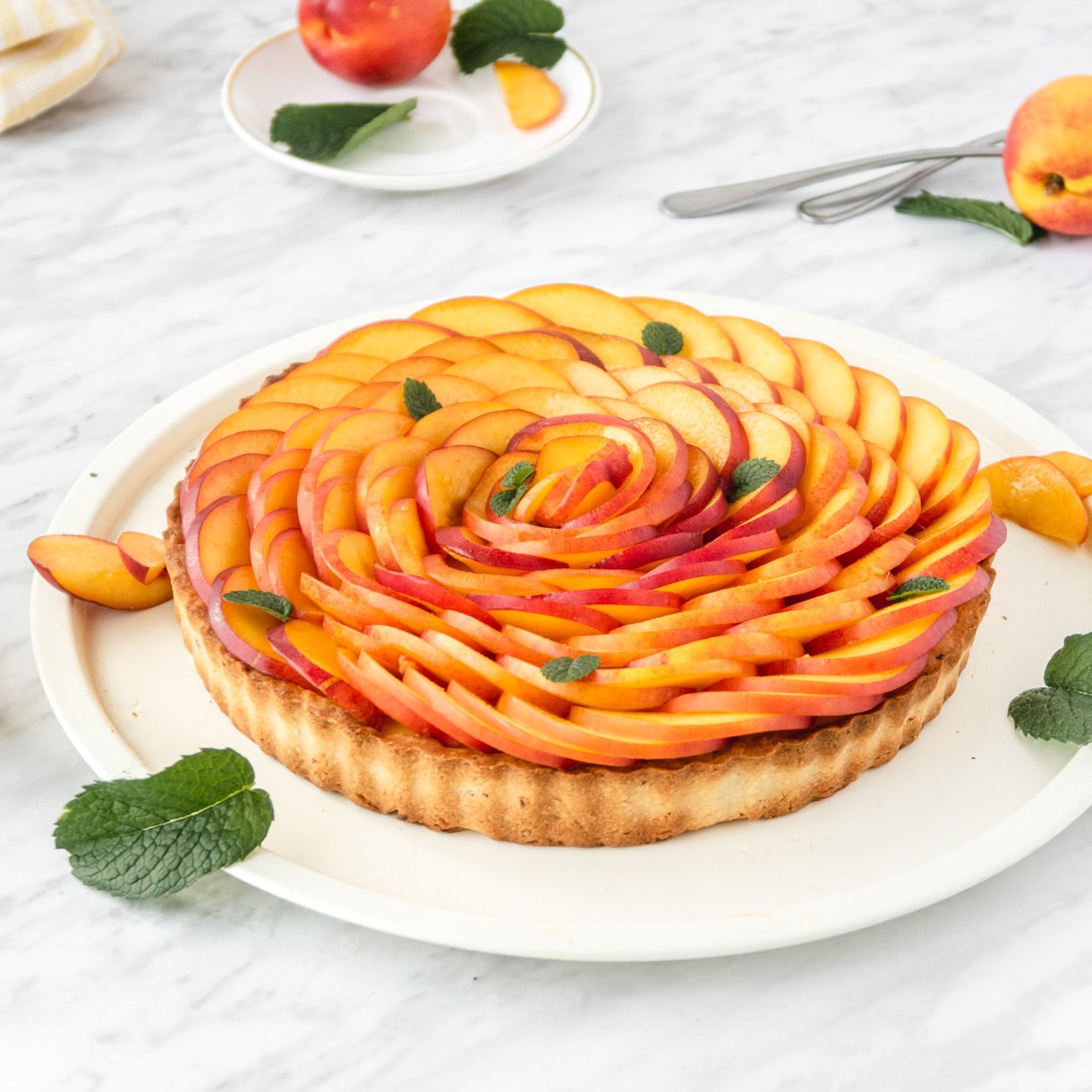 ¾ view of a nectarine tart on a white plate with mind leaves garnishes