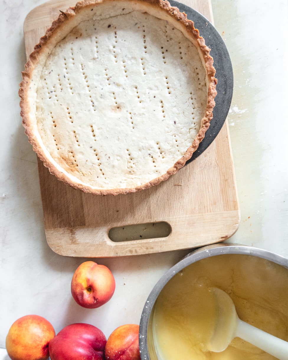 Top view of an empty tart shell and a saucepan of nectarine and passion fruit filling