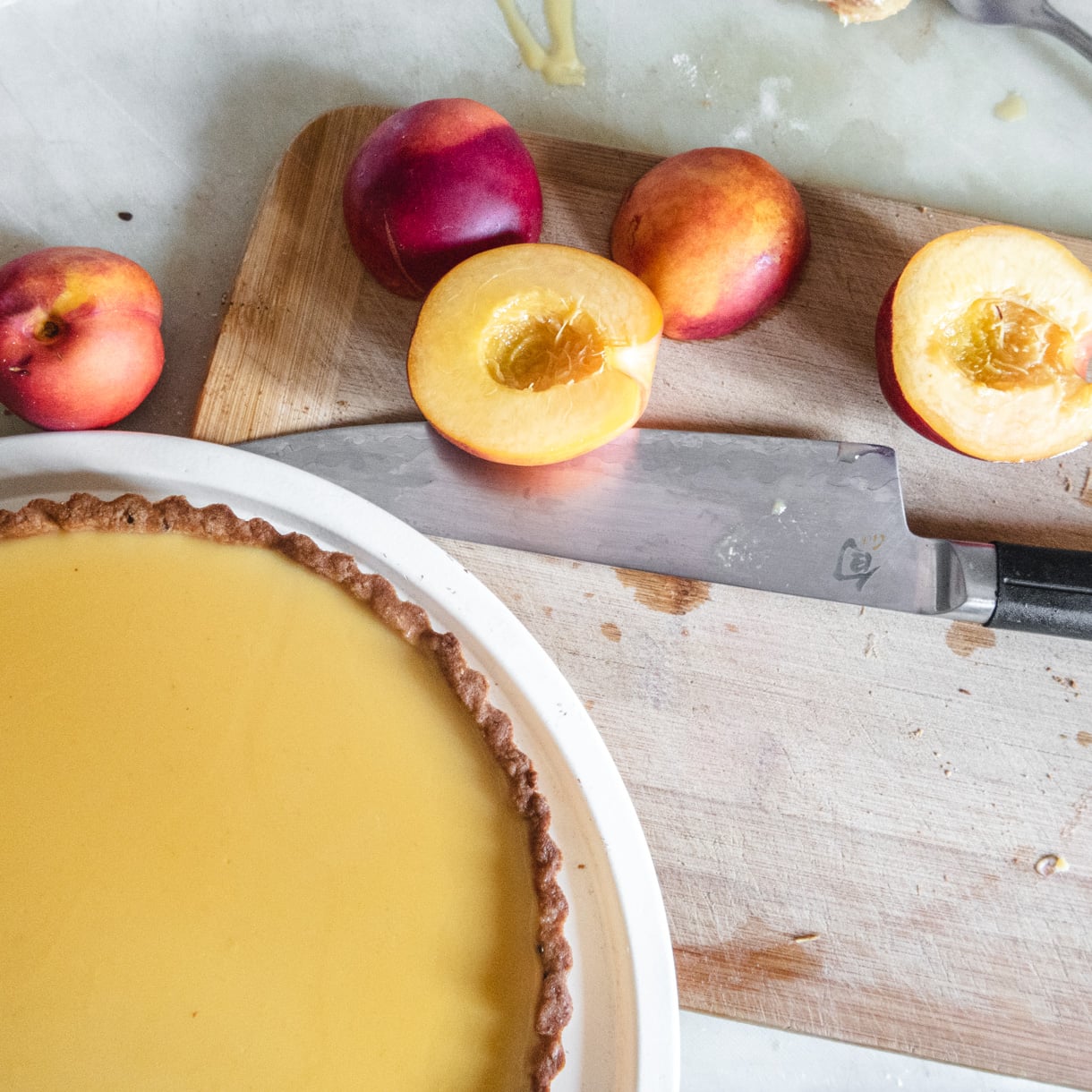 Fresh nectarines sliced in half over a cutting board with the pie in the foreground