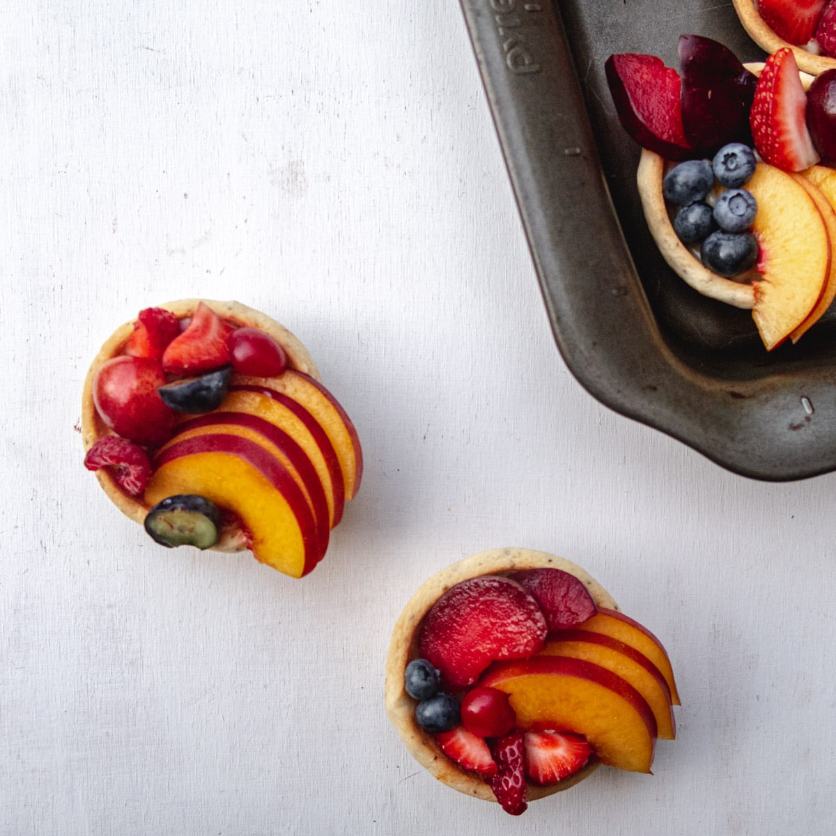 top view of 2 vegan fresh furit tartlets with custard on a white background