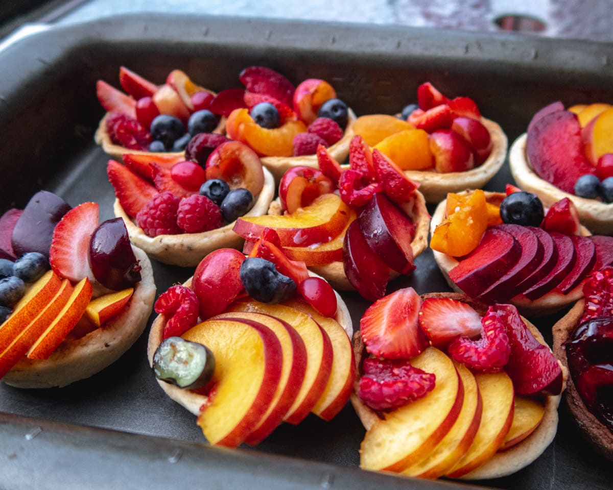 side view of a lot of vegan fresh fruit tartlets in a baking pan