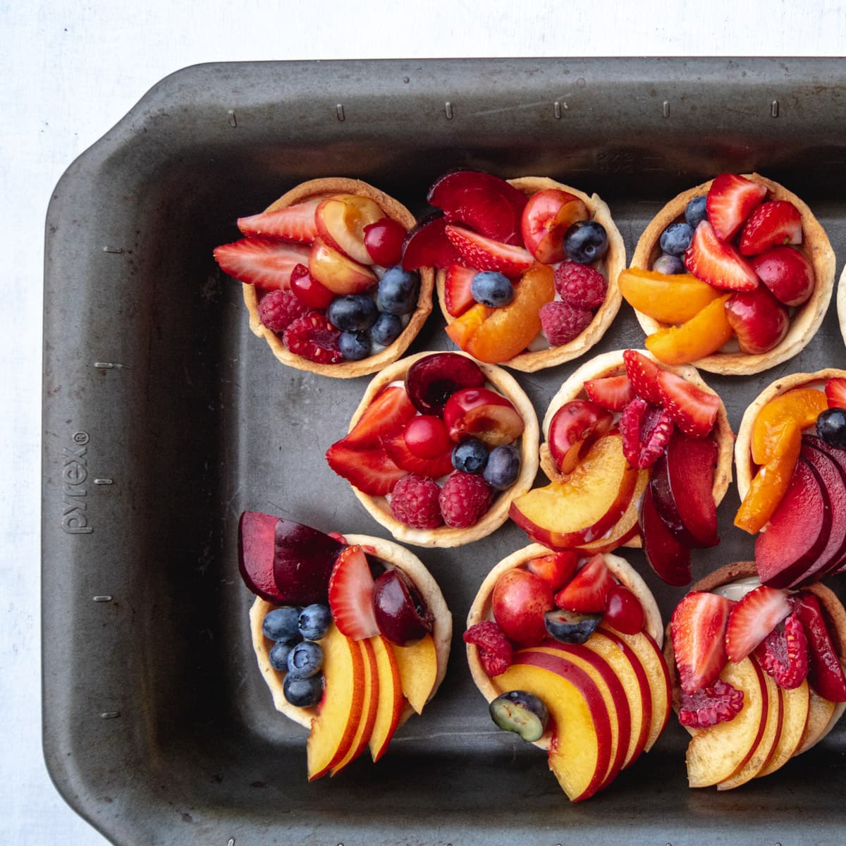 top down view of 9 fresh fruit and custard tartlets in a dark baking pan