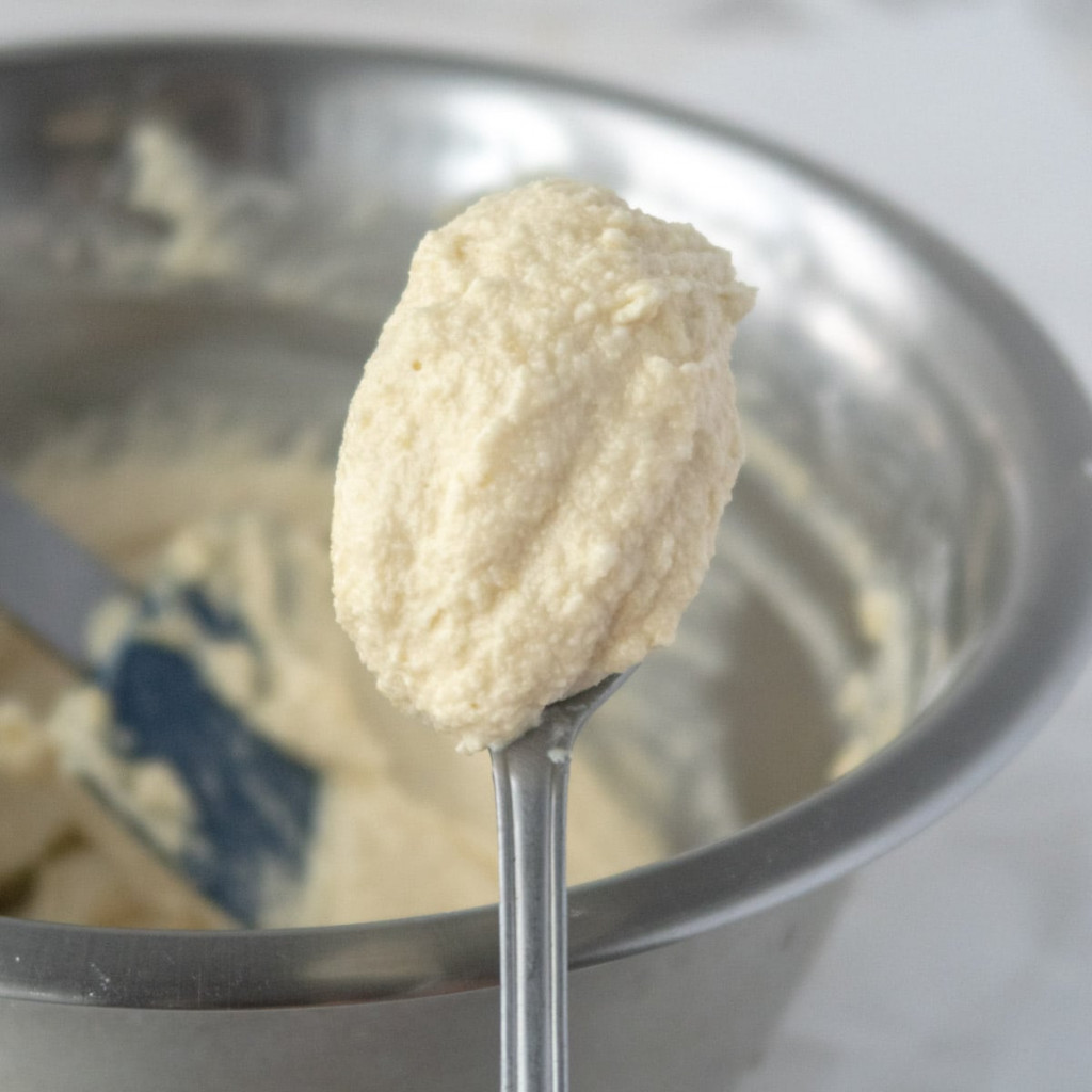 Vegan frangipane cream on a spoon in front of a metal bowl