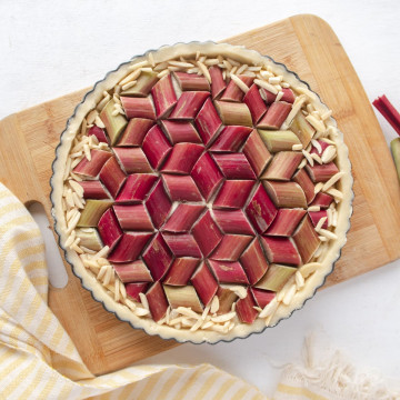 Top down view of a uncooked tart on a cutting board with a geometric rhubarb pattern on top of the tart