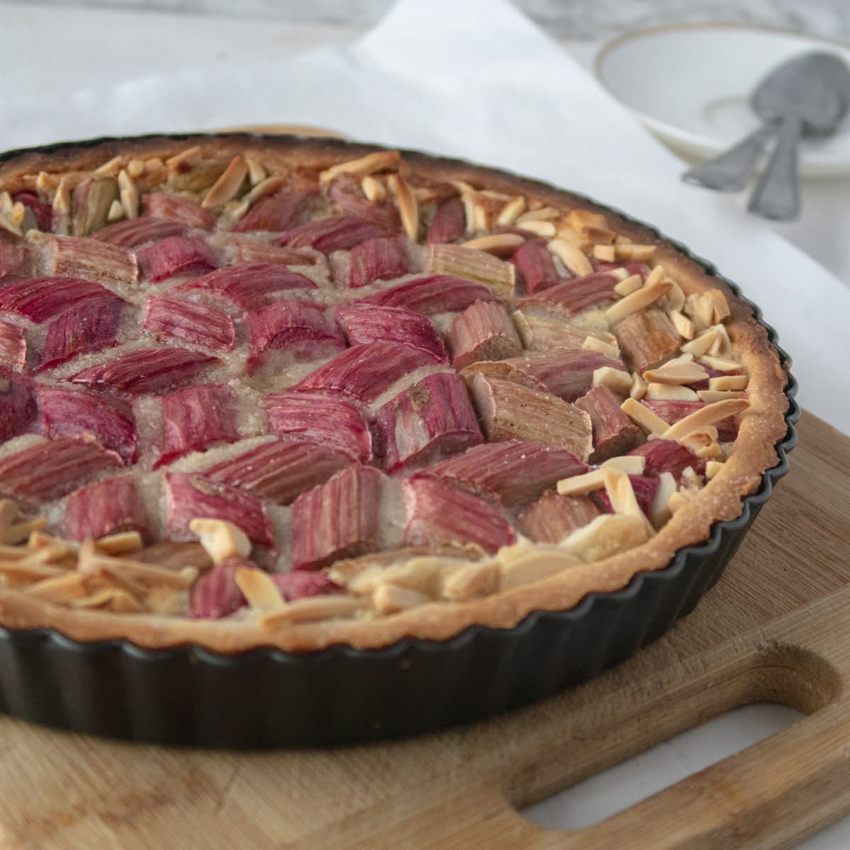 side view of a cooked vegan rhubarb and frangipane tarts with a closeup on sliced almonds that are on the edges