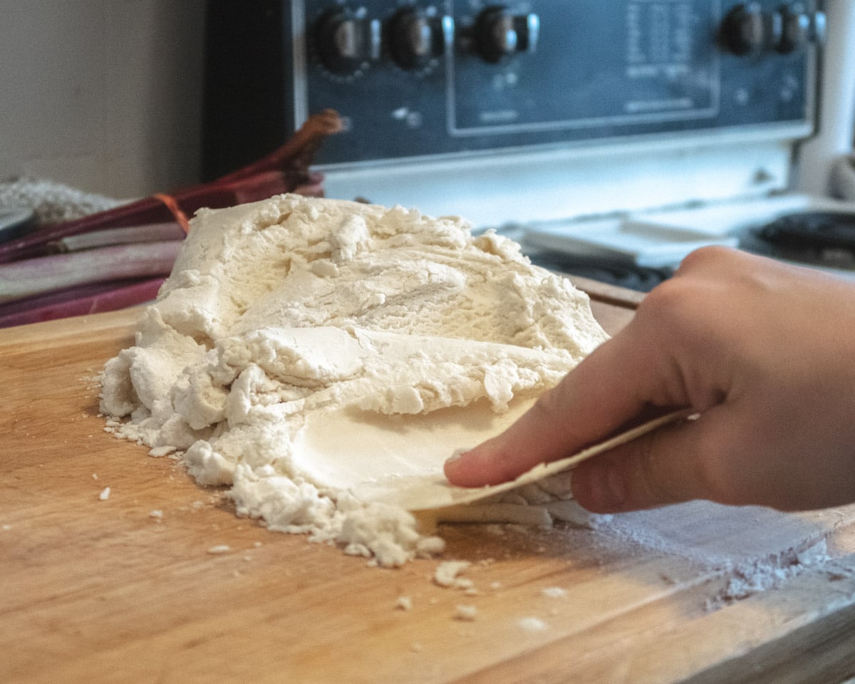 vegan pastry dough being squished with a bench scraper onto a wooden cutting board ( fraiser technique)