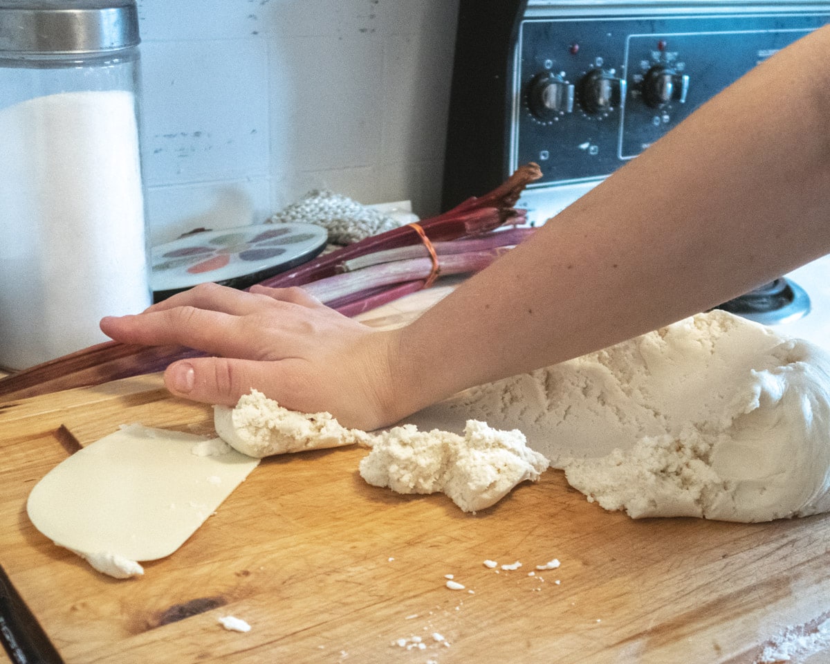 vegan pastry dough being pushed by the palm of the hand onto a wooden cutting board ( fraiser technique)