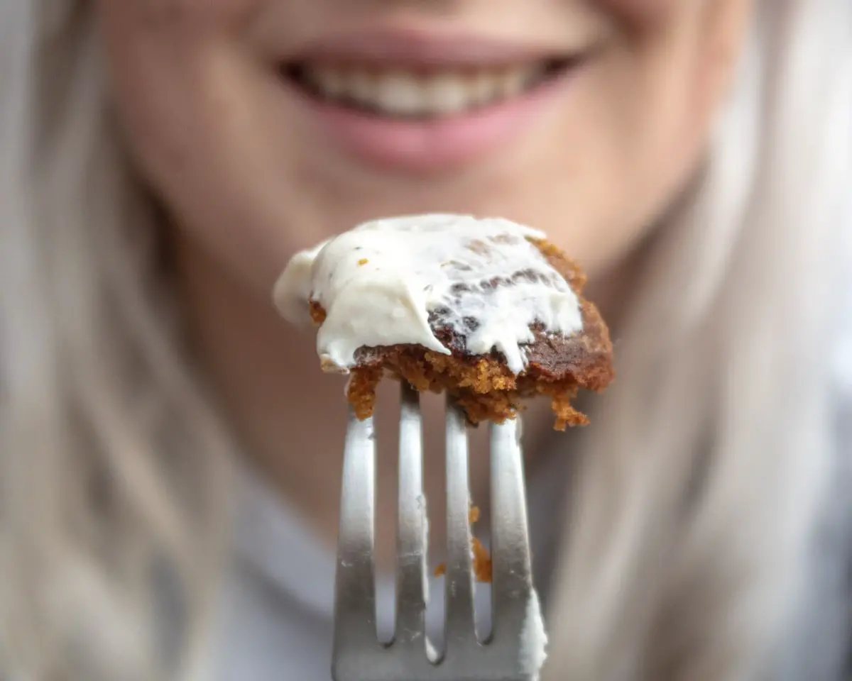 A piece of cake on a fork held in front of a blurry face in the background