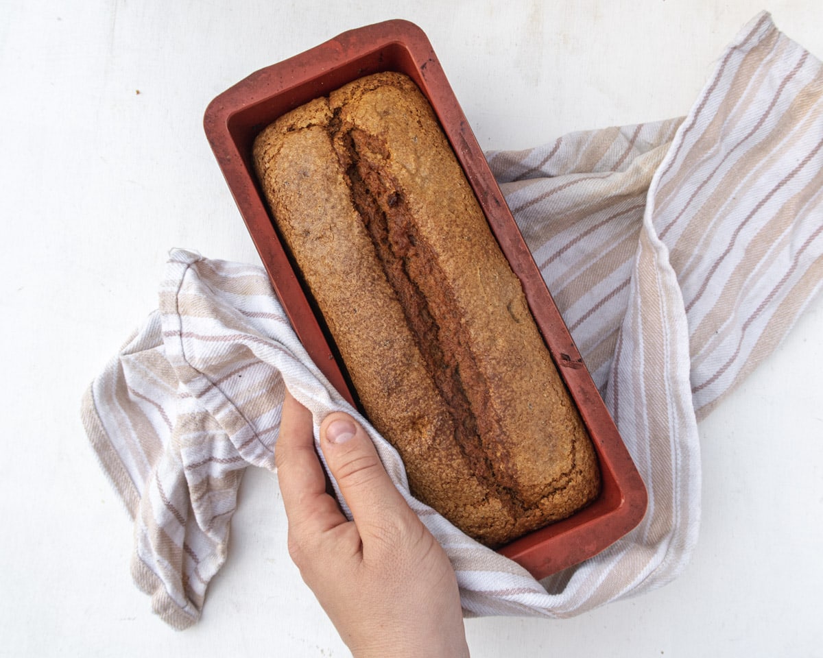 Vegan Bourbon pumpkin bread in the pan, wrapped in a dish towel