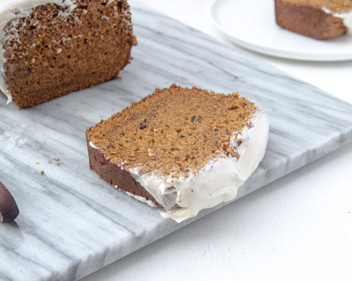 Vegan pumpkin bread slice on a marble serving plate with the while loaf in the background