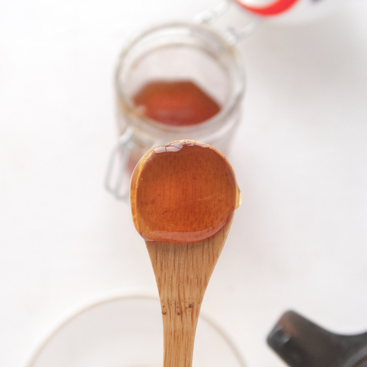 vegan honey on a bamboo spoon with the jar blurry in the backgorund