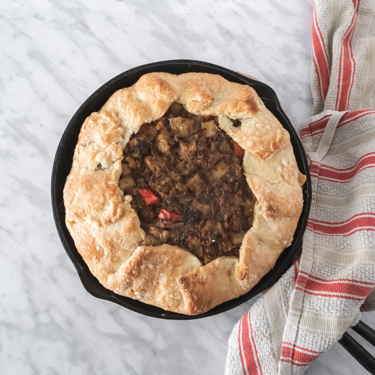 top down view of a rustic chickpea pie on a white background with a red-stripped dishtowel