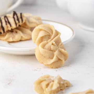 Danish butter cookies resting on a small plate with a teapot in the background