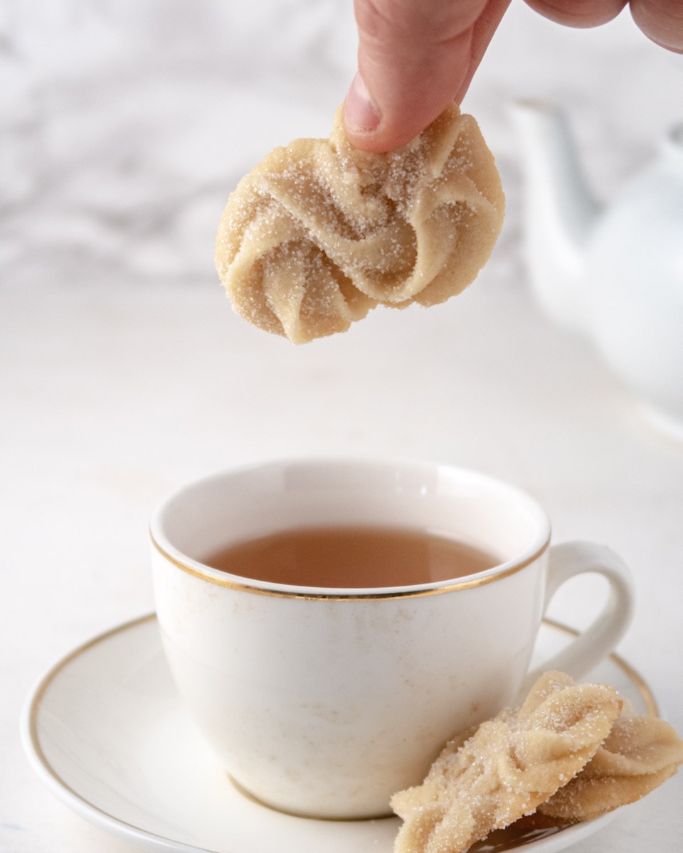 Vegan Danish butter cookie held by 2 fingers on top of a cup of tea