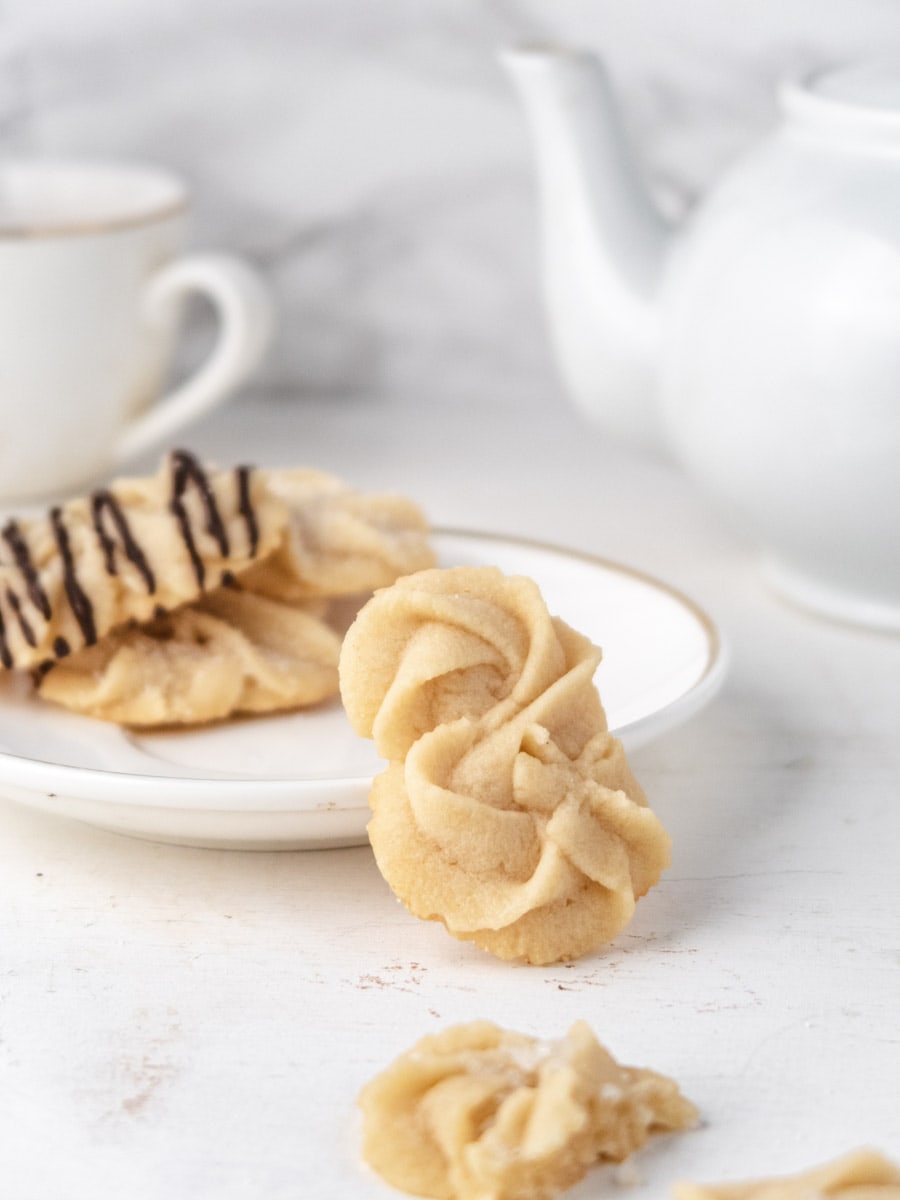 Danish butter cookies resting on a small plate with a teapot in the background