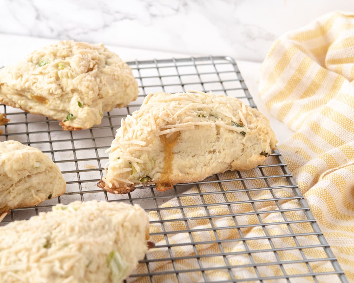 vegan herb and cheddar savoury scones on a wire cooling rack with a yellow-stripped dishtowel