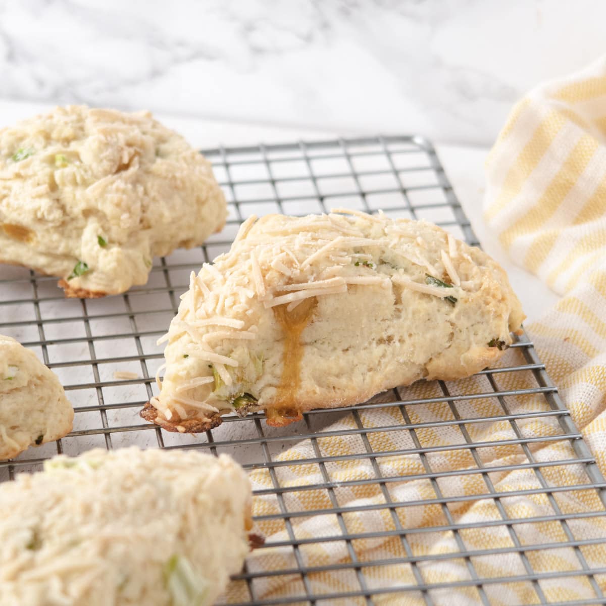 vegan herb and cheddar savoury scones on a wire cooling rack with a yellow-stripped dishtowel