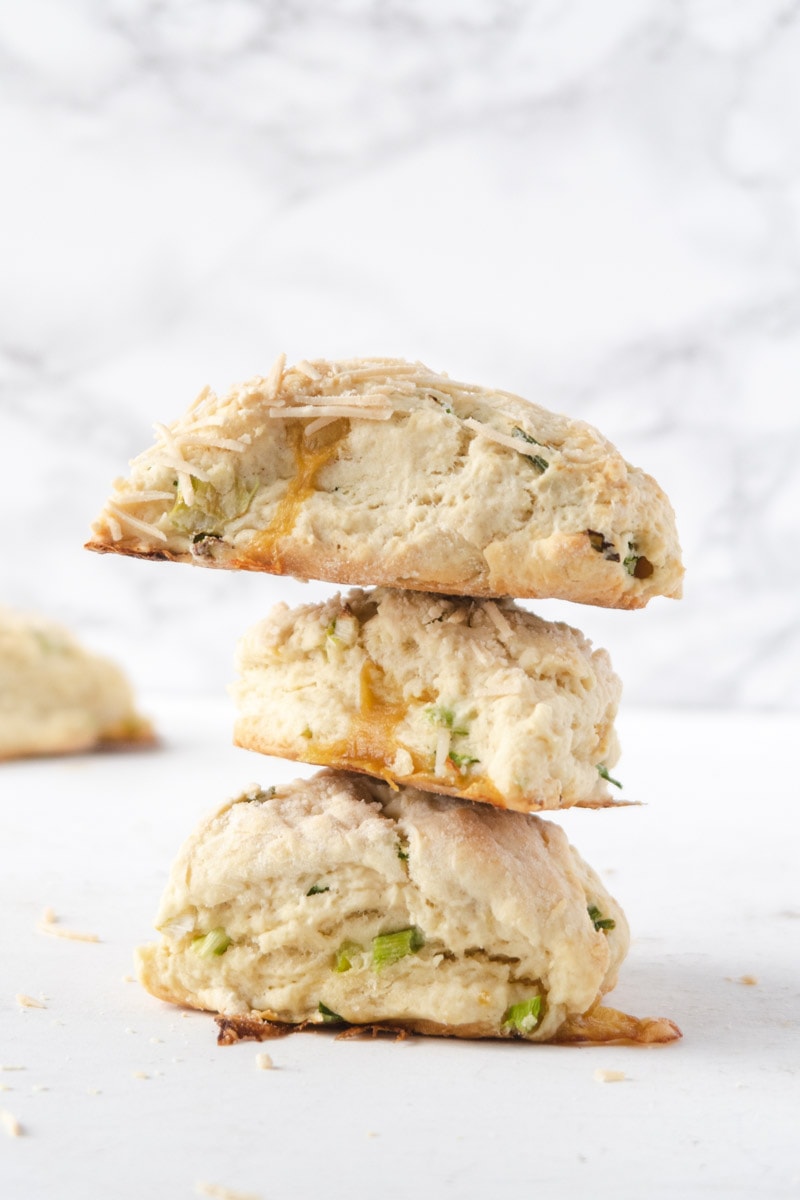 3 vegan herb and cheddar scones stacked on top of each other in front of a white and marbled background