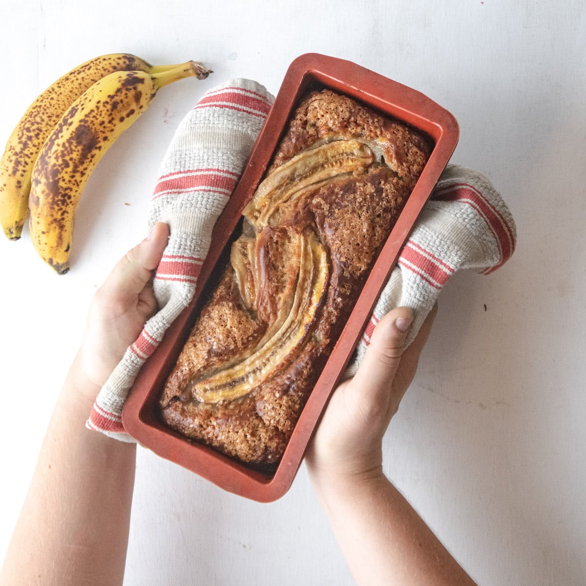 top view of a freshly baked banana loaf held up by 2 hands