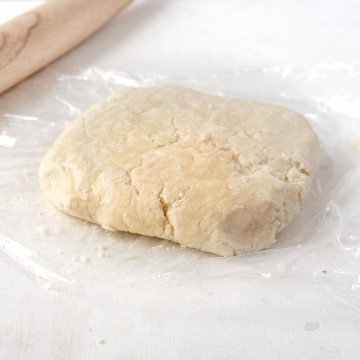 vegan pate brisee dough on a piece of plastic wrap with a rolling pin in the background