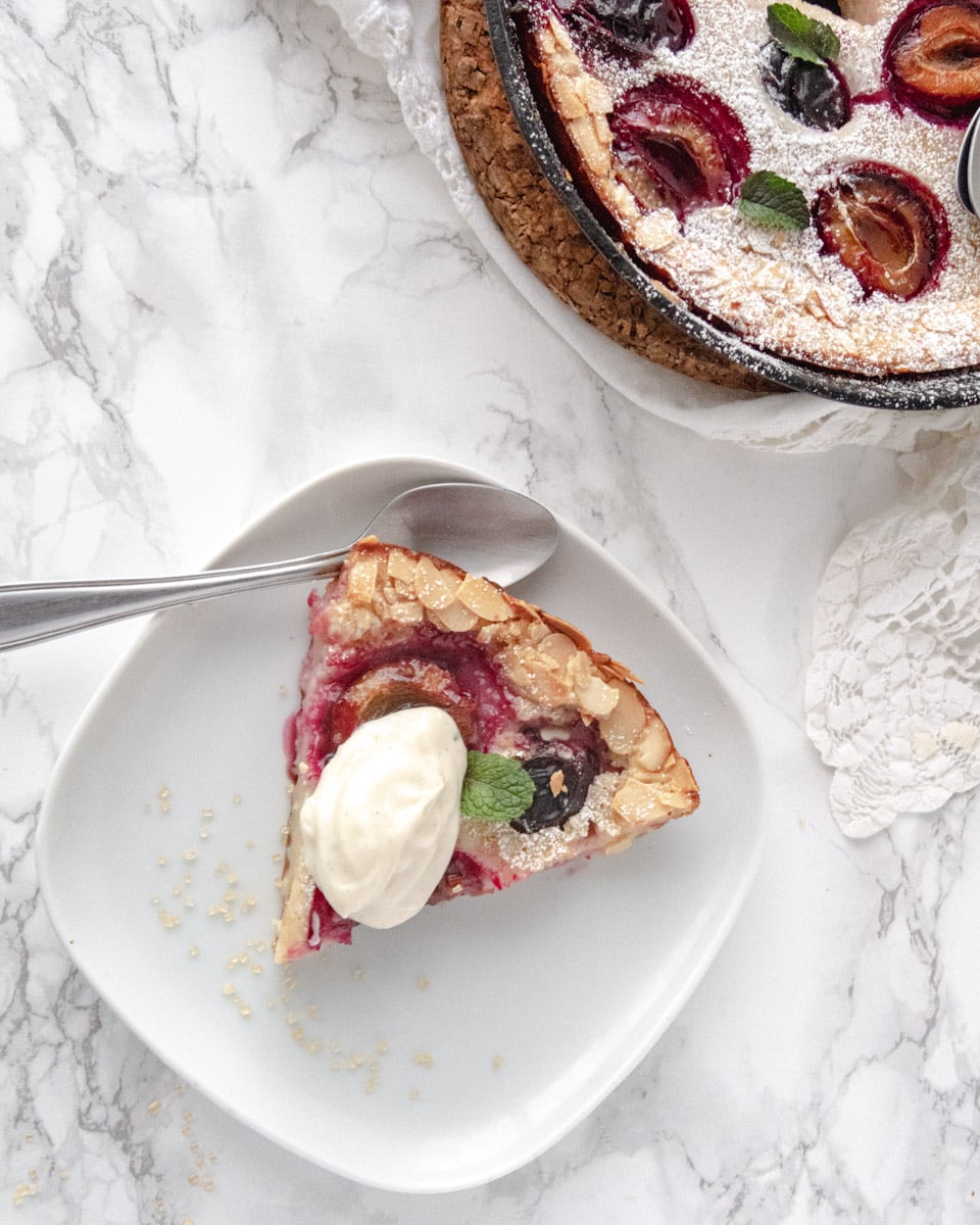 top down view of a slice of clafoutis on a plate with some cream on top