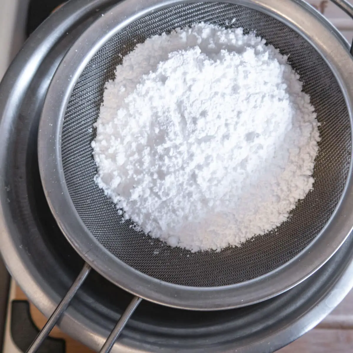 powderes sugar in a sieve on top of a bowl