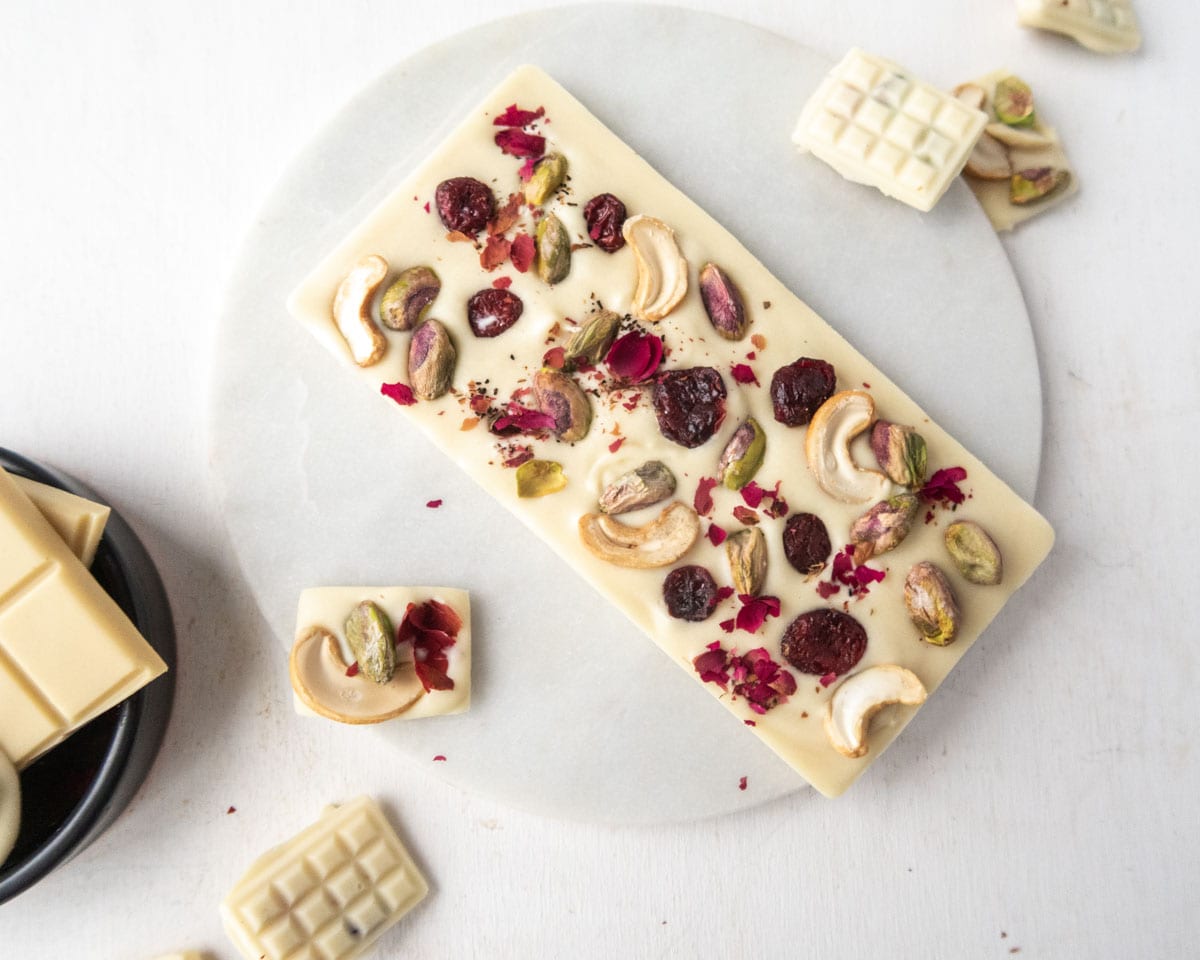 a large vegan white chocolate bar garnished with pistachioes, cashewes,dried cranberries and rose petals