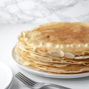 a tall stack of vegan crèpes on a plate with maple syrup in the background