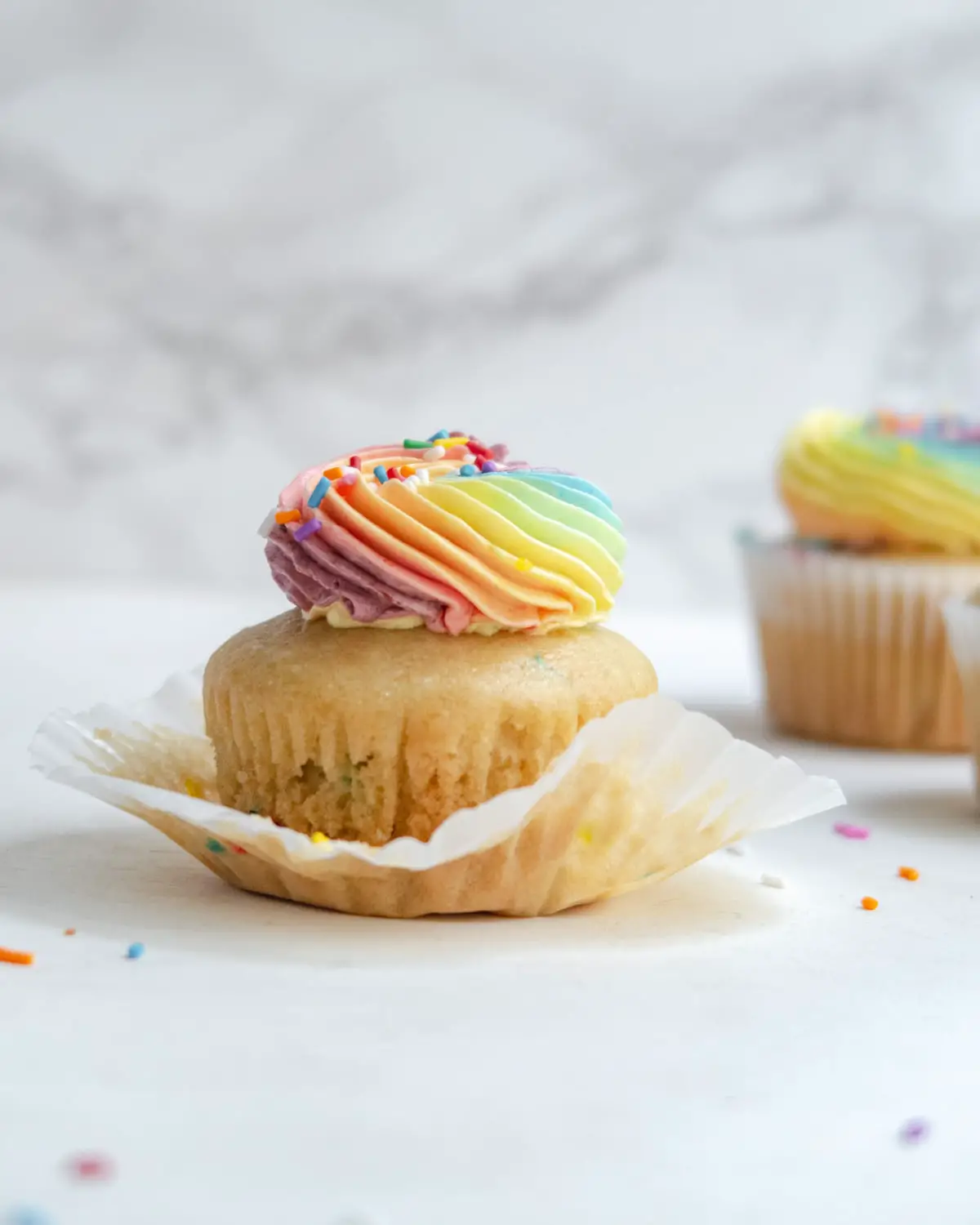 partially unwrapped cupcake with pastel rainbow icing