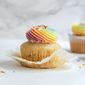 partially unwrapped vegan funfetti cupcake with pastel rainbow icing