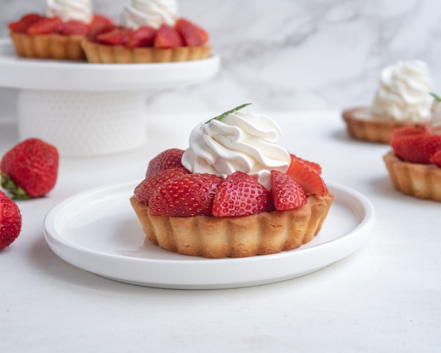 side view of a vegan fresh strawberry and rhubarb tartlets on a plate with more tartlets in the background 