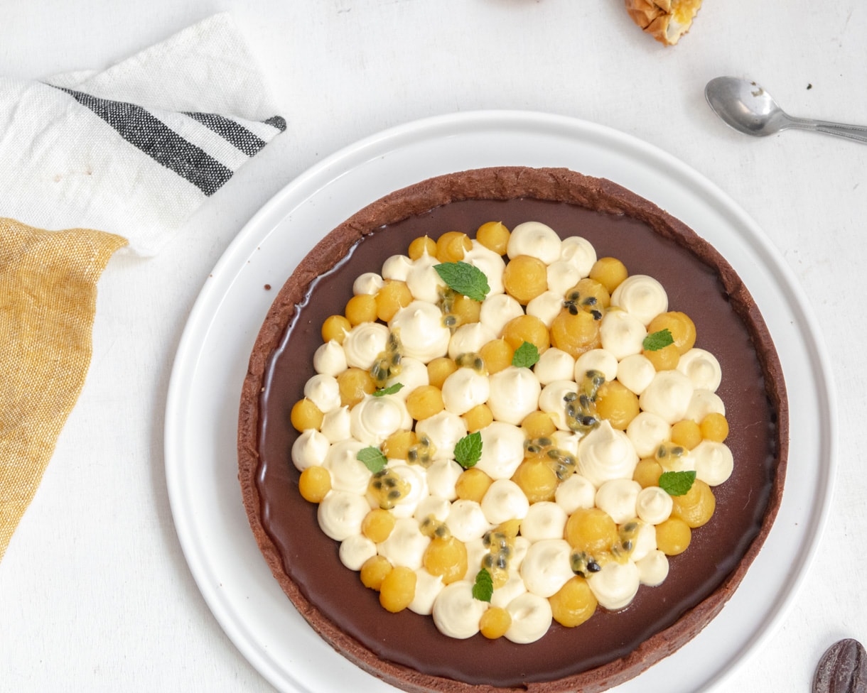 top down view of the vegan passionfruit and chocolate tart on a white plate next to a mustard and gray stripped dishtowel 