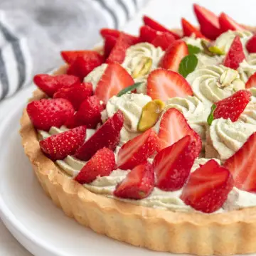 side view of a partial pistachio and strawberry tart on a white plate