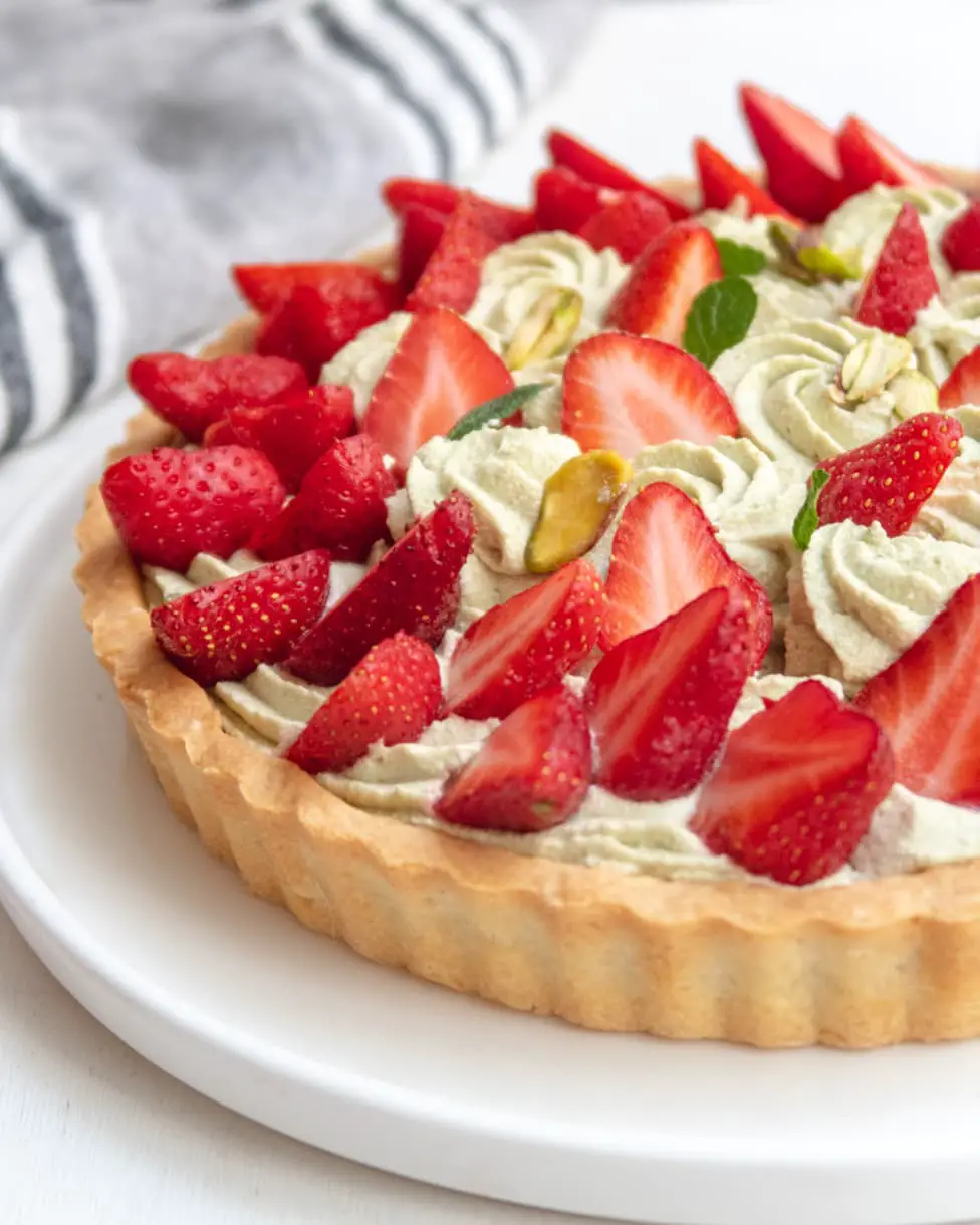 side view of a partial pistachio and strawberry tart on a white plate