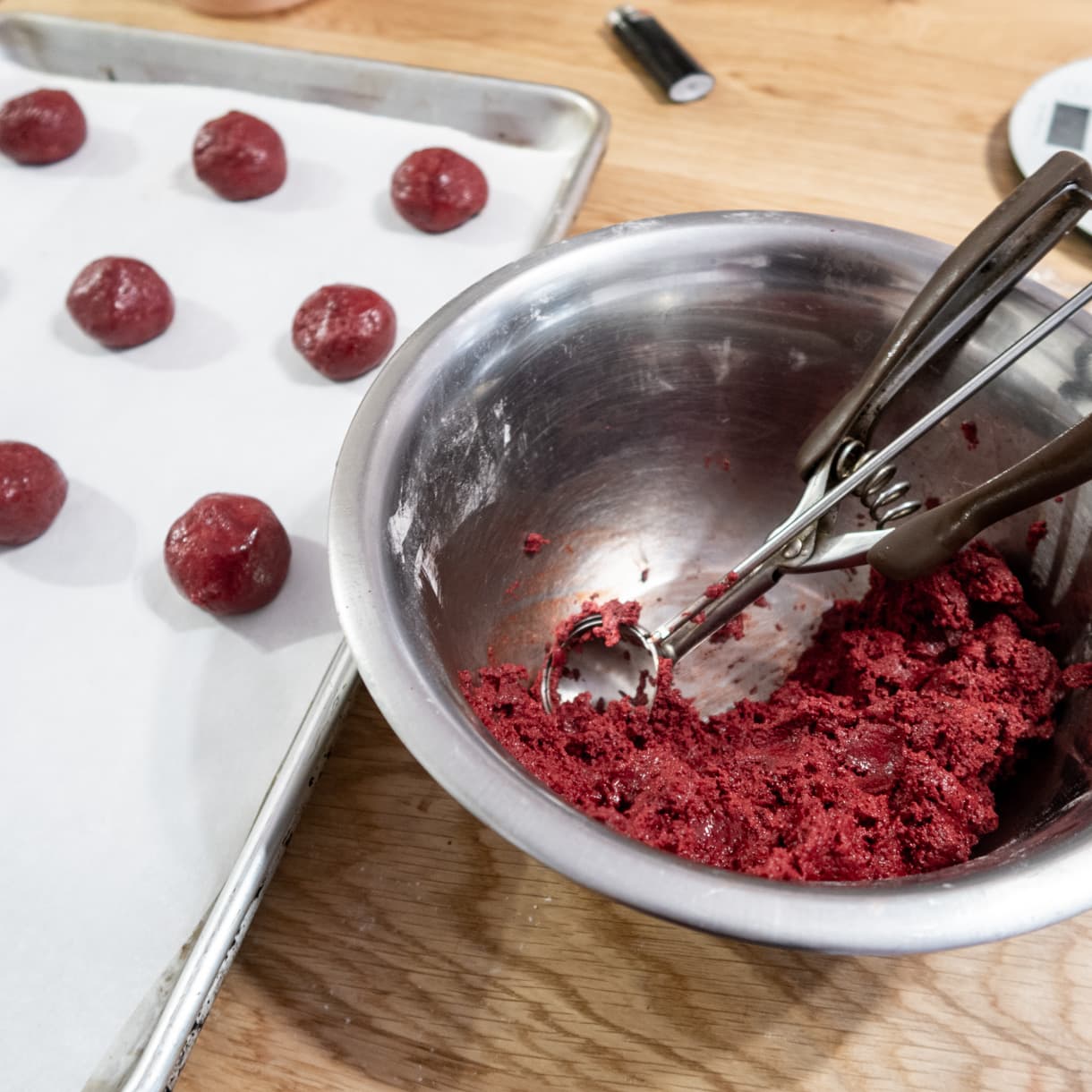 Red velvet cookies being scooped with an ice scream spoon on a baking sheet.