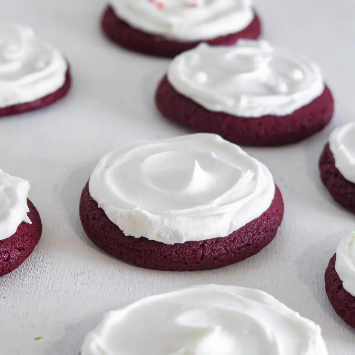 An assortment of vegan red velvet lofthouse-style cookies iced with cream cheese icing on a white background.