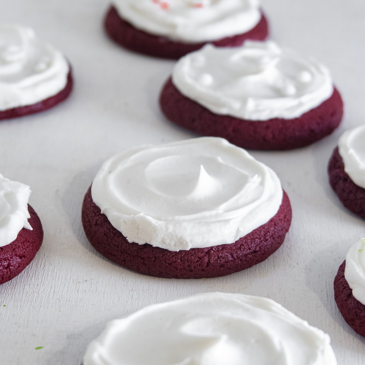 an assortment of vegan red velvet lofthouse-style cookies iced with cream cheese icing on a white background.