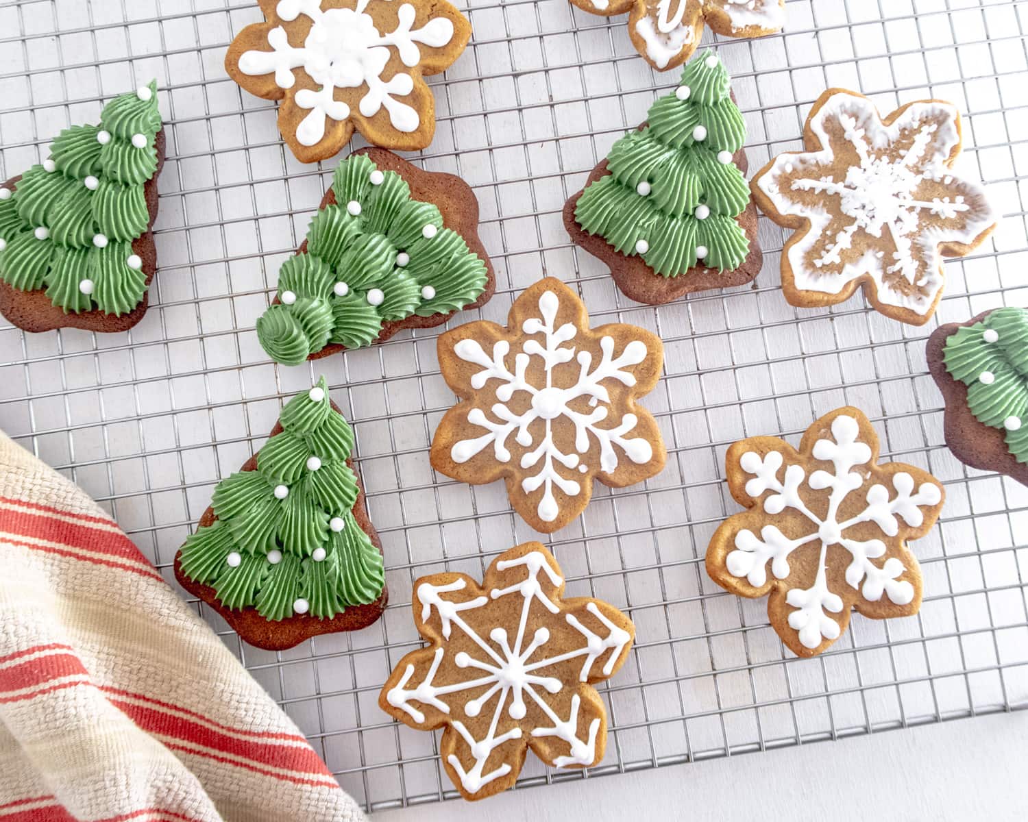 a selection of gingerbread cookies ( christmas tree, gingerbread person and snow flake) decorated with vegan royal icing on a wire drying rack