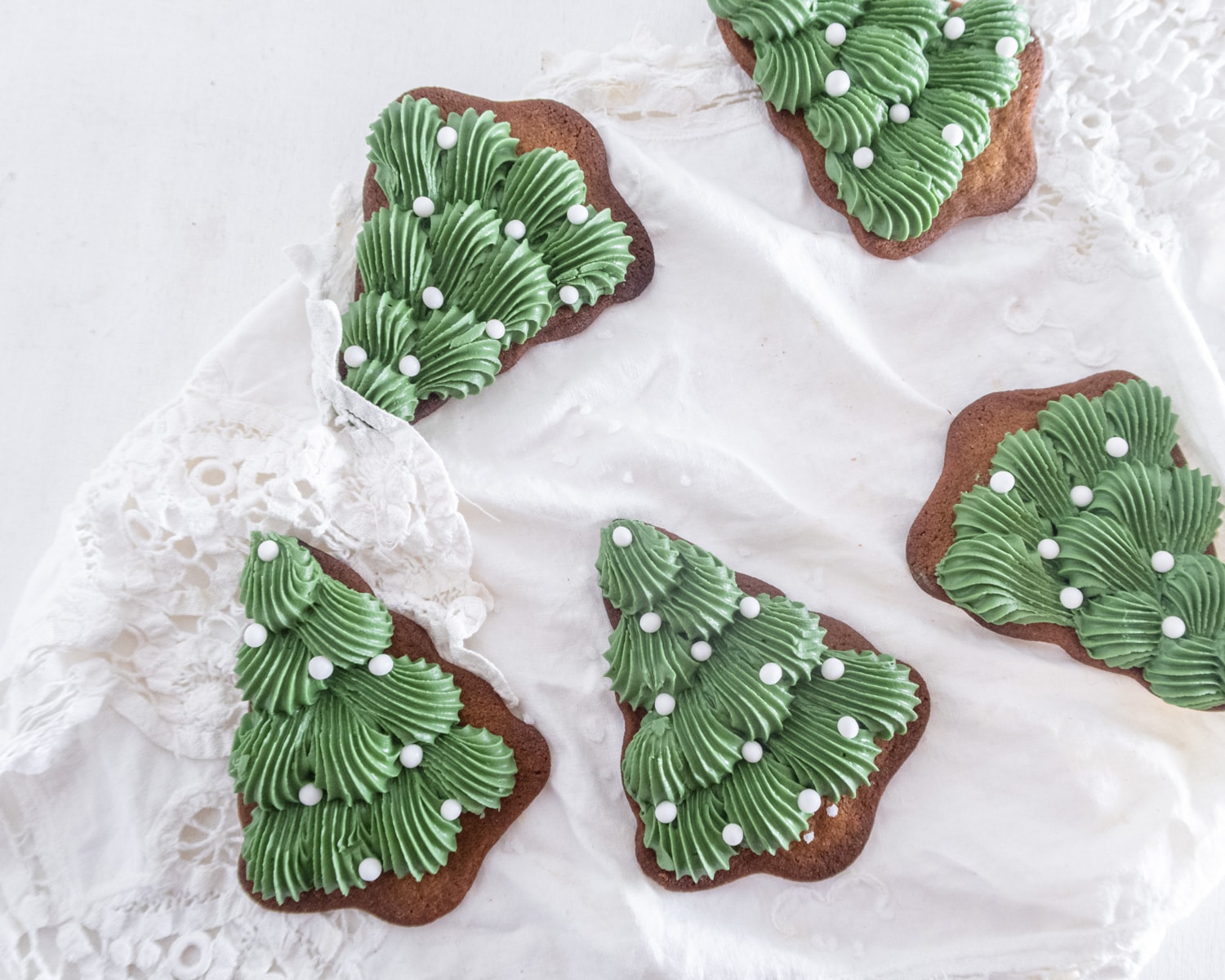 5 decorated gingerbread tree cookies on top of a white lace fabric