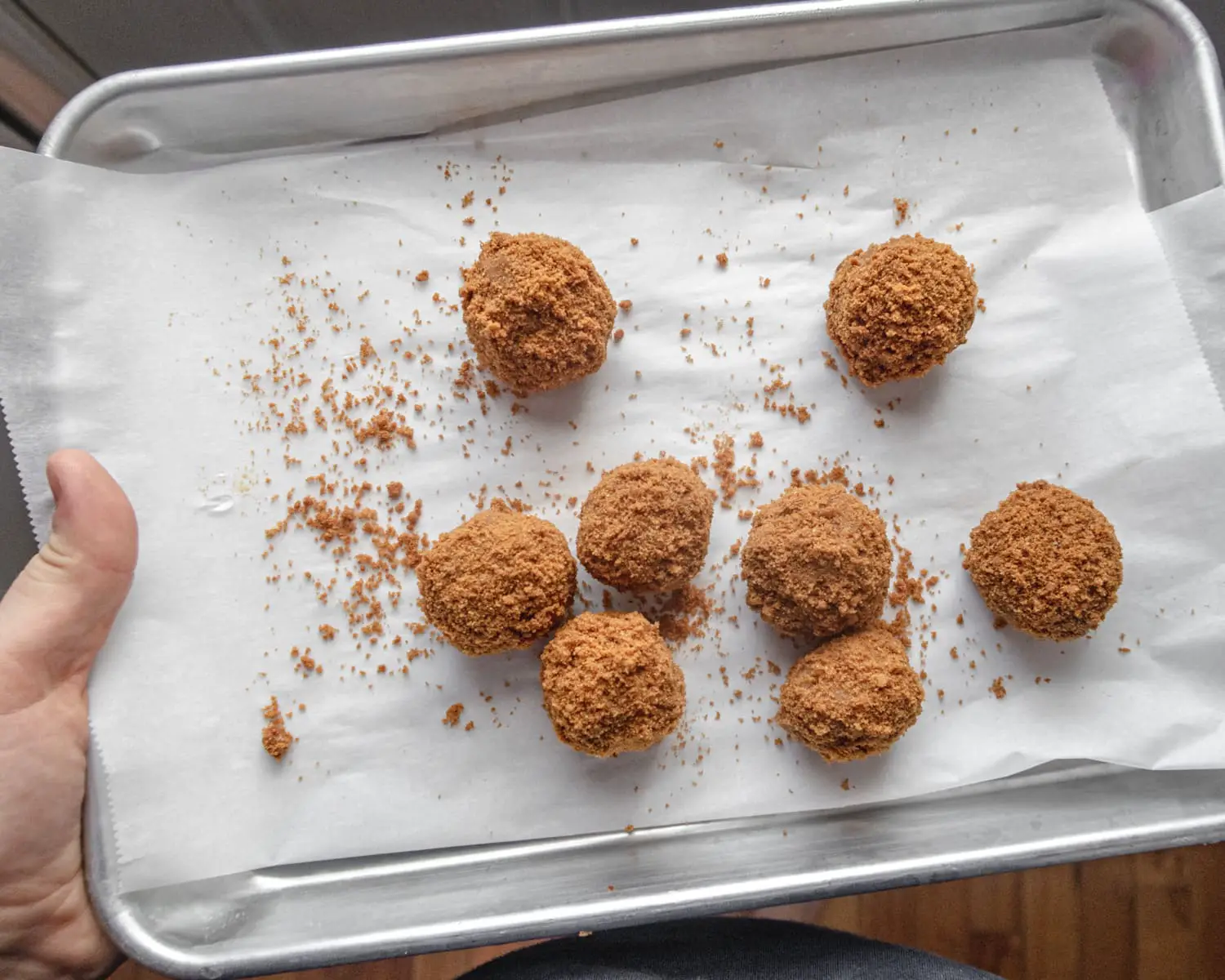 Biscoff cake truffles rolled in cookie crumbs being held on a small baking tray.