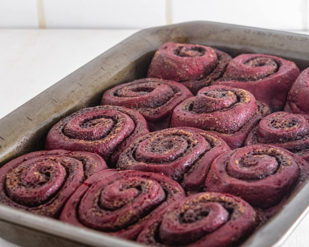 Closeup of 12 vegan red velvet cinnamon rolls without icing on a baking dish.