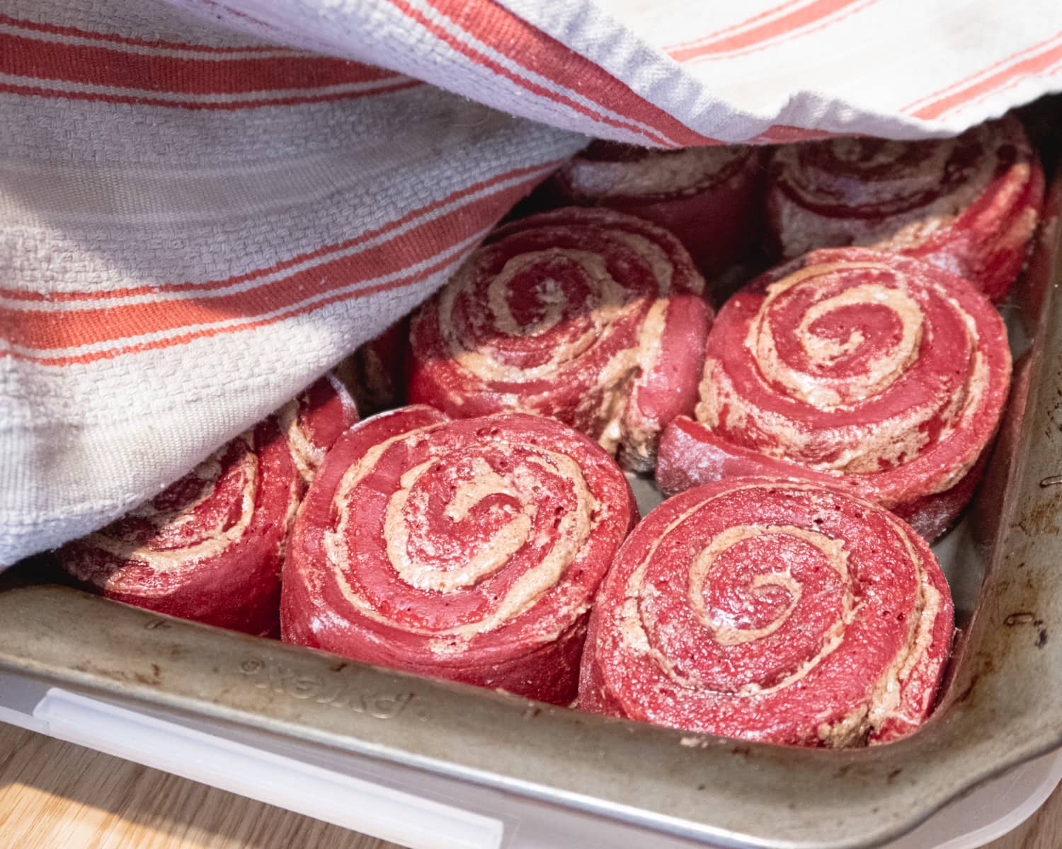 Raw vegan red velvet cinnamon rolls mid proofing half covered with a dish towel.