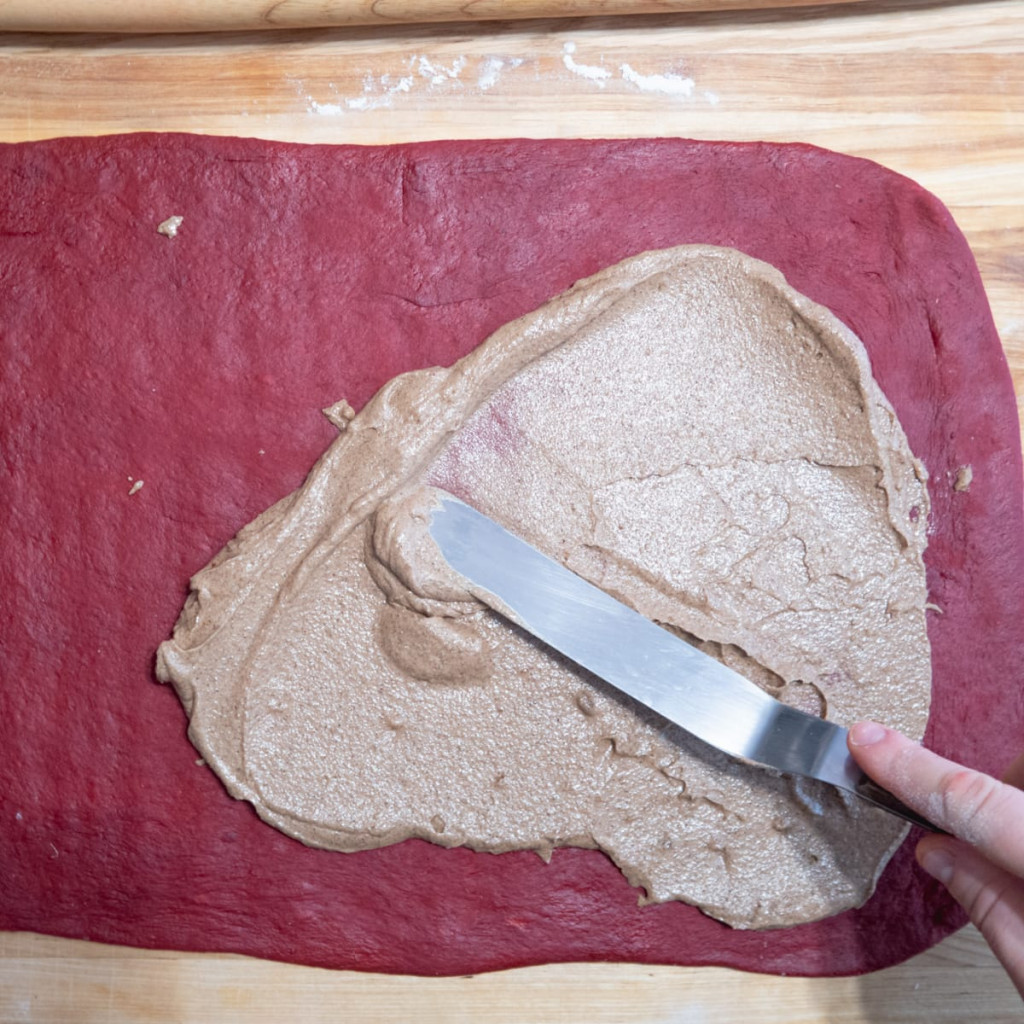 Cinnamon filling being spread on a rectangular rolled red dough.