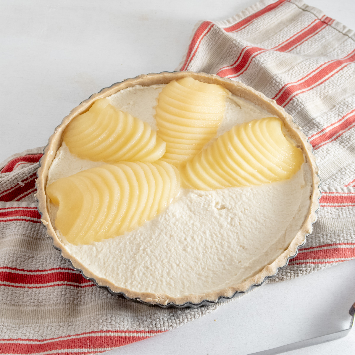 Sliced pears being placed on top of almond cream for a Bourdaloue tart.