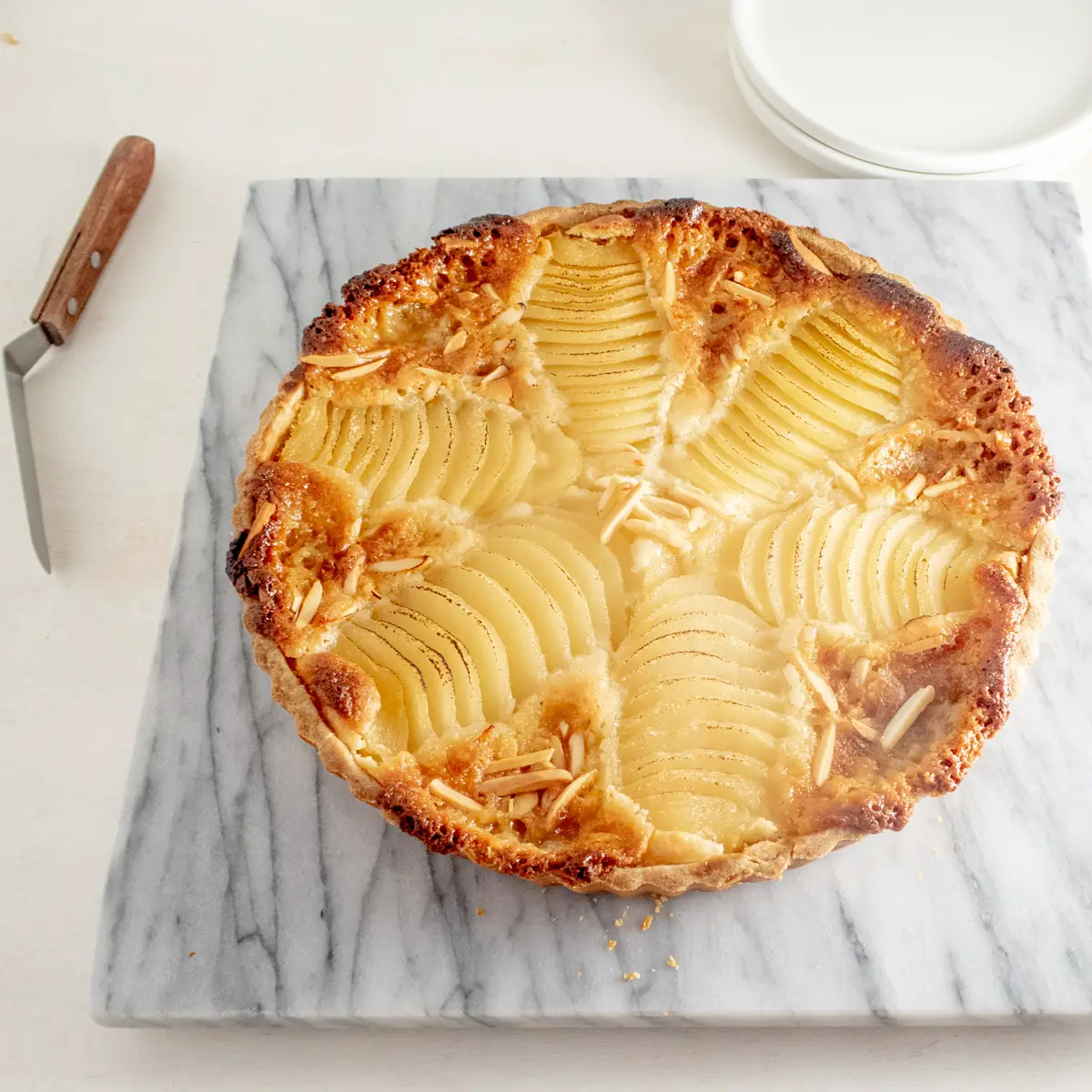 Vegan pear and almond cream tart on a marble slab with plated and a small offset spatula in the background.