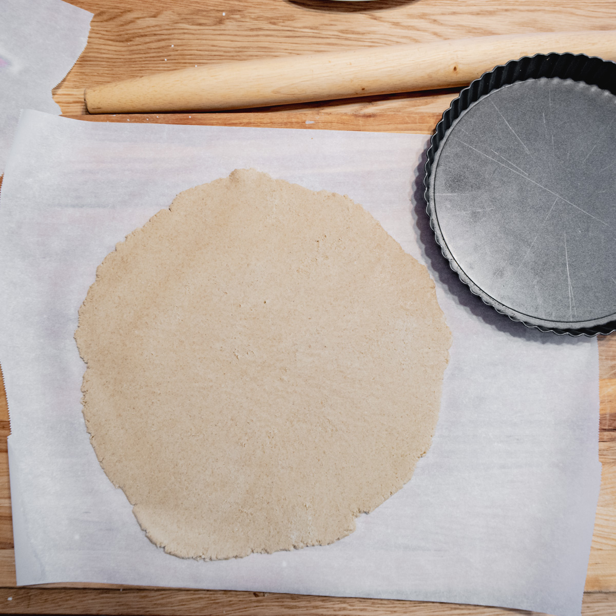 Gluten-free pâte sucrée rolled out into a circle with a fluted tart tin on the side.