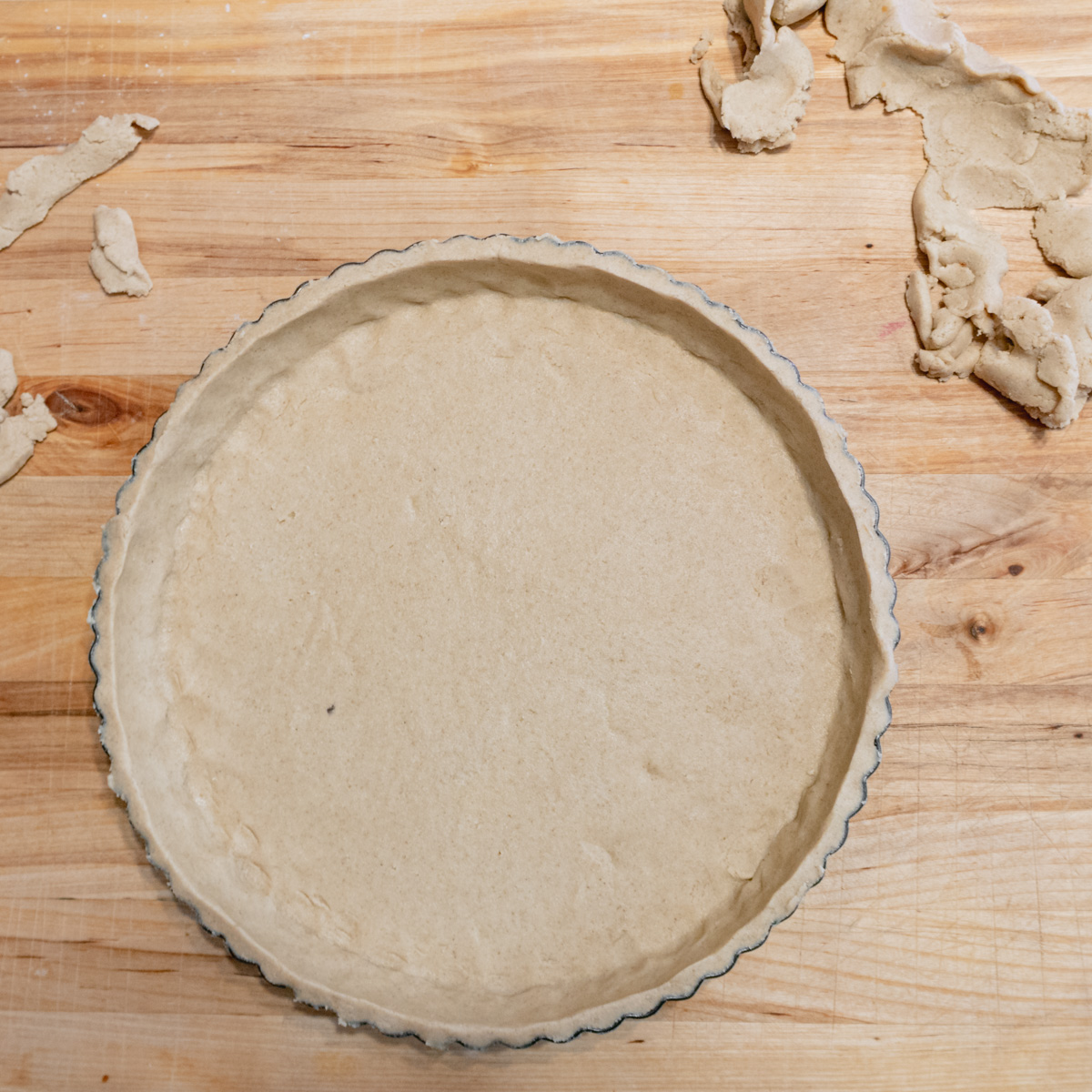 Tart tin lined with raw gluten-free pastry dough with cutoffs around it..